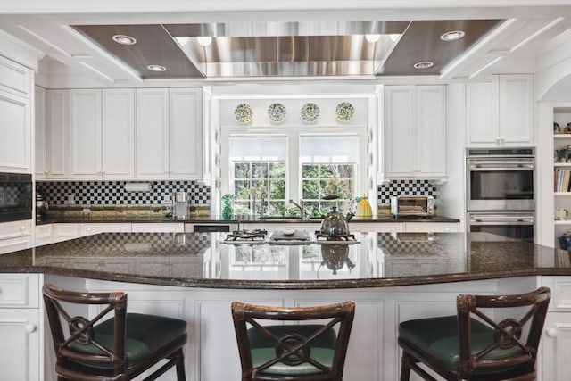 135 Marsh St, Belmont, MA 02478 - kitchen with a kitchen bar, appliances with stainless steel finishes, tasteful backsplash, white cabinets, and wall chimney exhaust hood