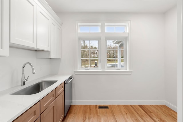 kitchen with dishwasher, light stone counters, sink, white cabinets, and light hardwood / wood-style flooring