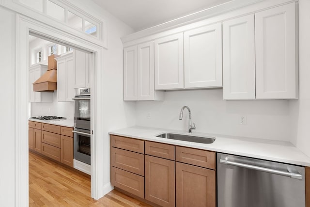 kitchen with white cabinets, stainless steel appliances, light wood-type flooring, custom exhaust hood, and sink