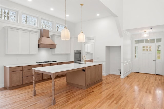 kitchen with white cabinets, a center island with sink, plenty of natural light, and custom range hood