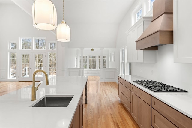 kitchen featuring light wood-type flooring, premium range hood, stainless steel gas stovetop, and a wealth of natural light