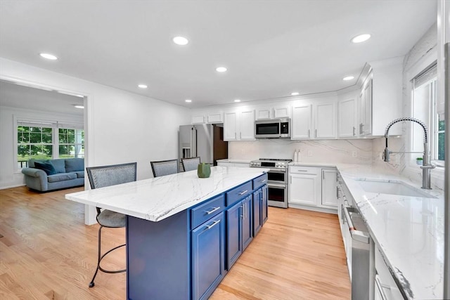 47 Fenwick Cir, Methuen, MA 01844 - kitchen with appliances with stainless steel finishes, blue cabinets, white cabinets, a breakfast bar, and light wood-type flooring