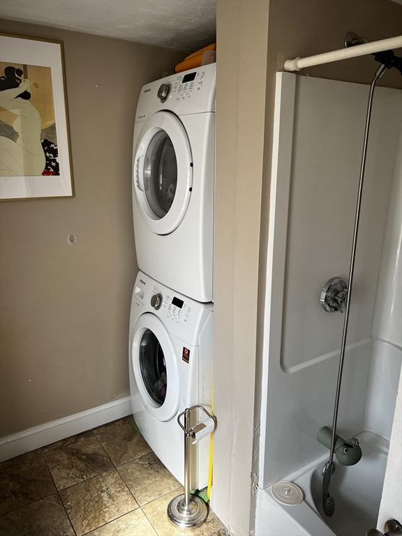 clothes washing area featuring laundry area, stacked washer / drying machine, and baseboards