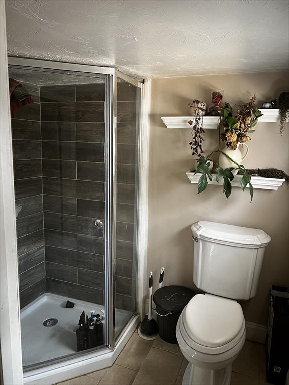 bathroom with tile patterned floors, baseboards, toilet, and a shower stall