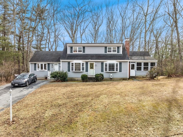 view of front of home with driveway, a chimney, a front yard, and a shingled roof