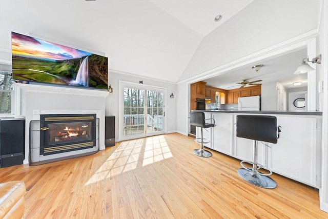 unfurnished living room featuring light wood-style flooring, lofted ceiling, a glass covered fireplace, and a ceiling fan