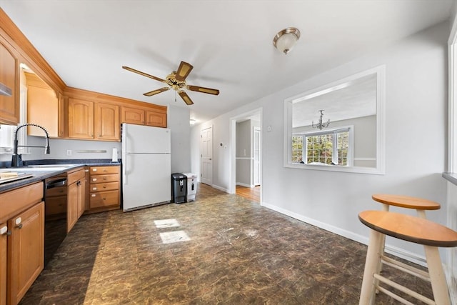 kitchen featuring dark countertops, baseboards, black dishwasher, freestanding refrigerator, and a sink