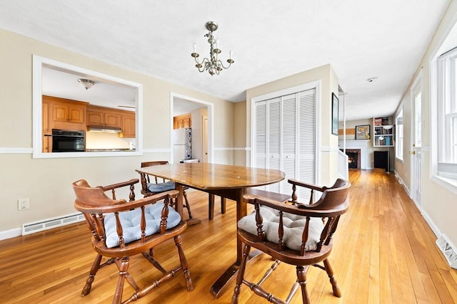 dining area with visible vents, a notable chandelier, a brick fireplace, and light wood-style flooring