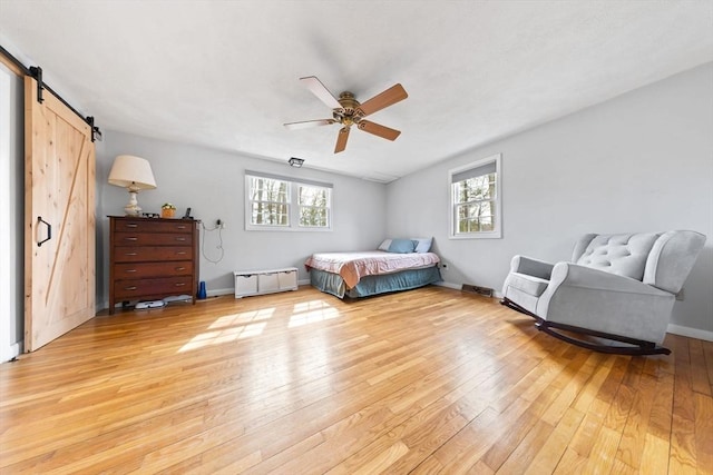 bedroom with baseboards, light wood-style floors, a barn door, and a ceiling fan