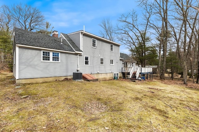 back of property featuring a yard, a shingled roof, a wooden deck, central AC unit, and a chimney