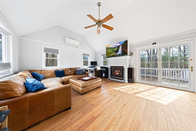 living area with a ceiling fan, high vaulted ceiling, a wall mounted AC, light wood-style floors, and a glass covered fireplace