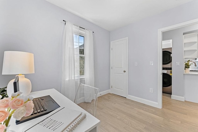 office with light wood finished floors, stacked washer / dryer, and baseboards