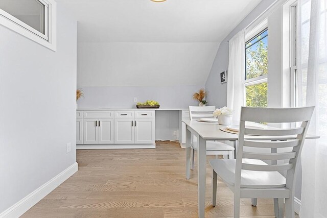 dining space featuring light wood-style floors, lofted ceiling, and baseboards