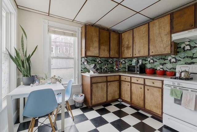 kitchen featuring light floors, light countertops, under cabinet range hood, stainless steel microwave, and white gas range