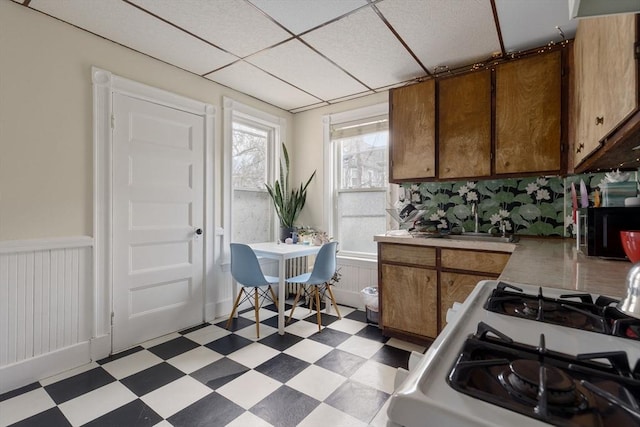 kitchen with light floors, white range with gas stovetop, wainscoting, and light countertops