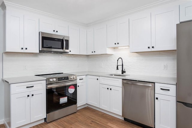 kitchen featuring light countertops, appliances with stainless steel finishes, white cabinetry, a sink, and wood finished floors