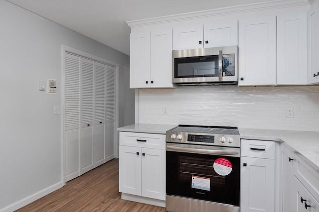 kitchen with tasteful backsplash, appliances with stainless steel finishes, light wood-style flooring, and white cabinets