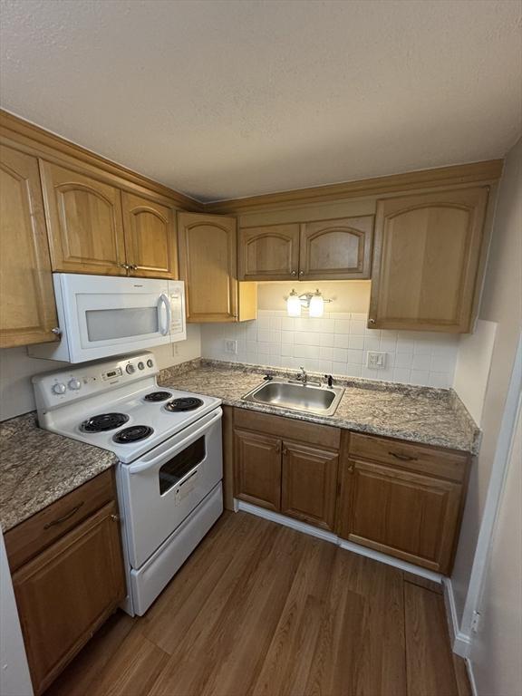 kitchen with dark hardwood / wood-style floors, light stone countertops, white appliances, and sink