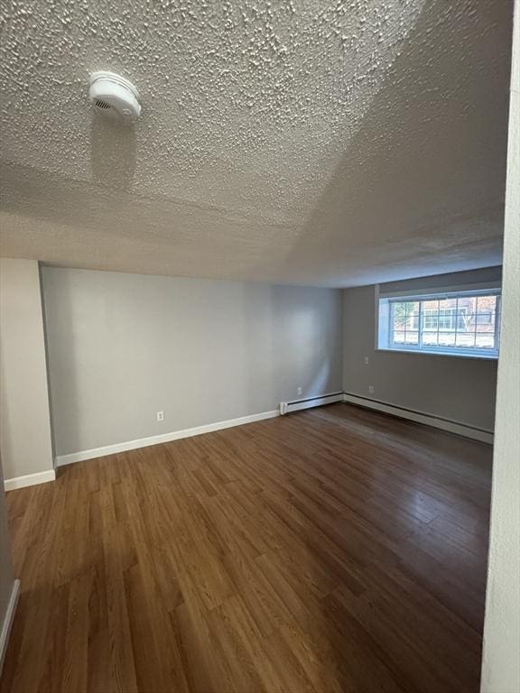 additional living space with a baseboard heating unit, a textured ceiling, and dark wood-type flooring