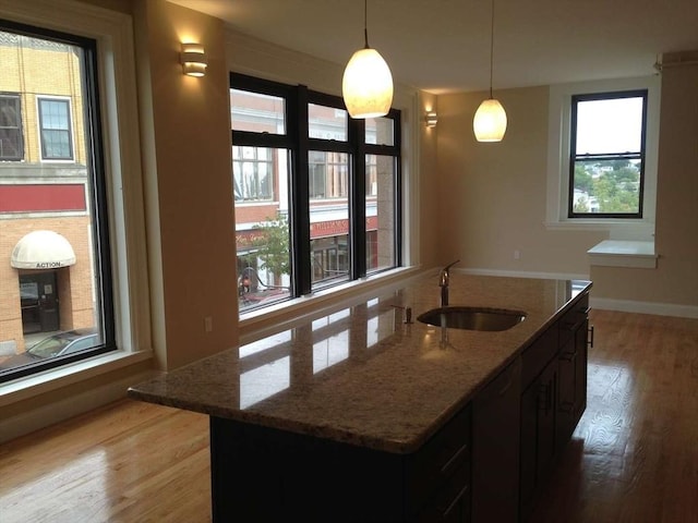 kitchen with a sink, dishwashing machine, light wood-style flooring, and stone counters
