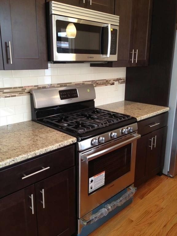 kitchen with stainless steel appliances, light wood-style floors, dark brown cabinetry, and tasteful backsplash
