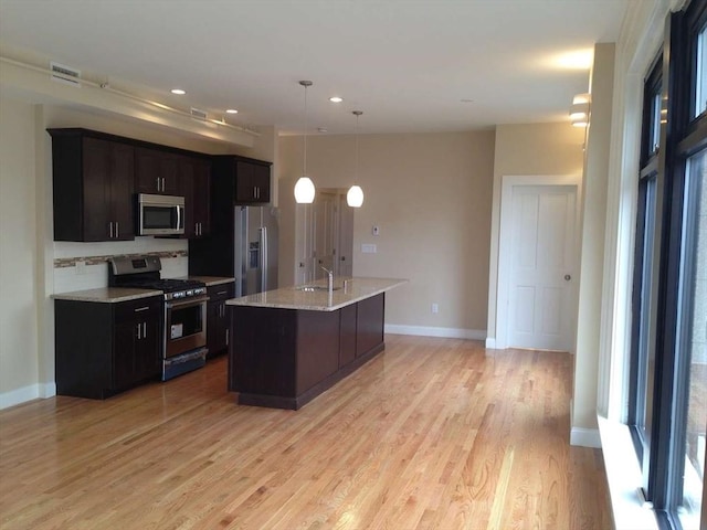 kitchen featuring stainless steel appliances, light wood-type flooring, backsplash, baseboards, and hanging light fixtures
