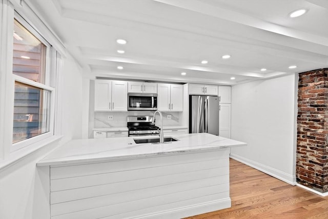 kitchen featuring white cabinetry, tasteful backsplash, kitchen peninsula, appliances with stainless steel finishes, and light wood-type flooring