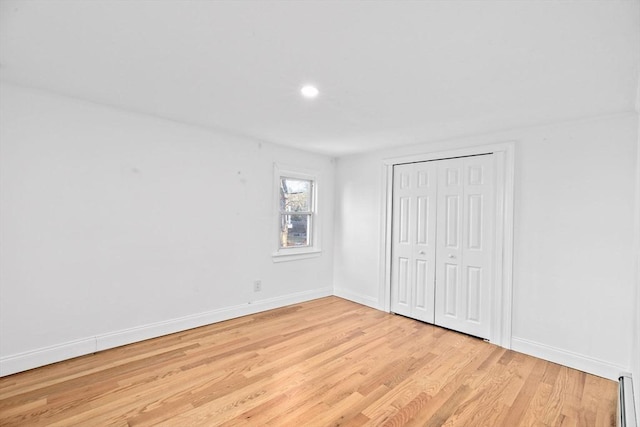 unfurnished bedroom with a closet, baseboard heating, and light hardwood / wood-style flooring