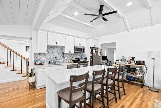 kitchen featuring vaulted ceiling with beams, white cabinetry, and appliances with stainless steel finishes