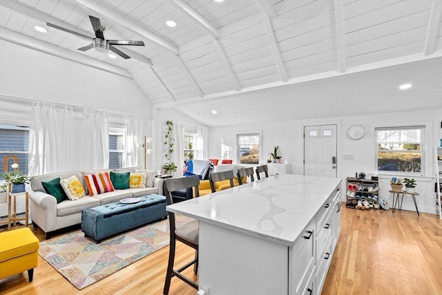 kitchen featuring a kitchen breakfast bar, ceiling fan, wooden ceiling, white cabinets, and vaulted ceiling with beams