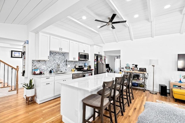 kitchen with a kitchen breakfast bar, white cabinets, lofted ceiling with beams, and appliances with stainless steel finishes