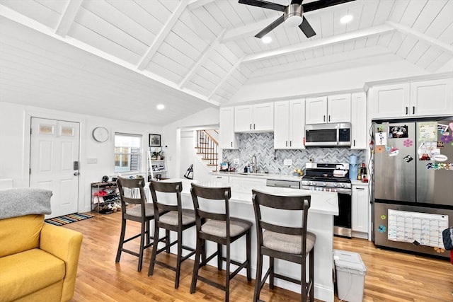 kitchen with tasteful backsplash, vaulted ceiling with beams, white cabinets, and appliances with stainless steel finishes