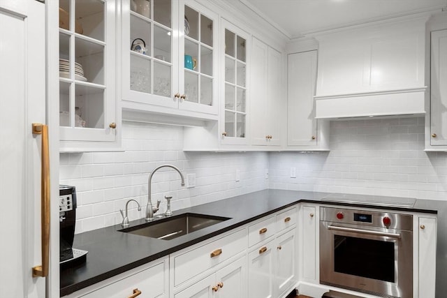 kitchen with dark countertops, oven, stovetop, white cabinetry, and a sink