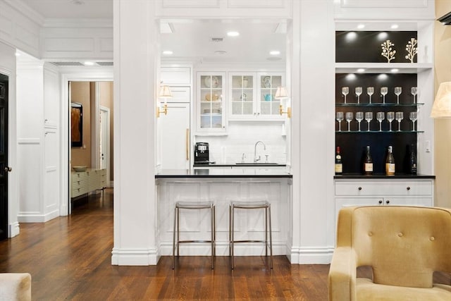 bar with backsplash, dark wood finished floors, wet bar, paneled built in refrigerator, and a sink