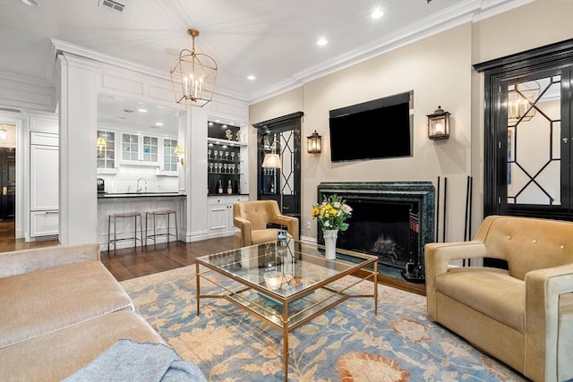 living area featuring wood finished floors, a fireplace with flush hearth, recessed lighting, ornamental molding, and indoor wet bar