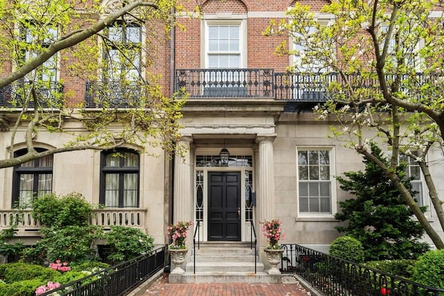 property entrance featuring a balcony, brick siding, and stone siding