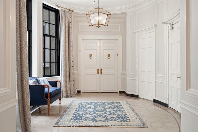 entryway with a chandelier, ornamental molding, and a decorative wall