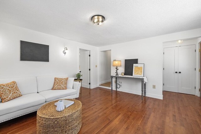 living room with dark wood-style flooring, a textured ceiling, and baseboards