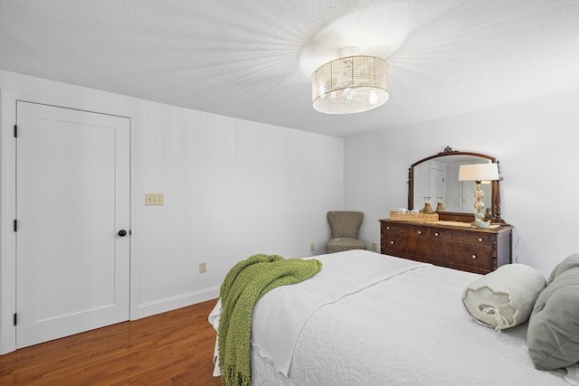 bedroom featuring a textured ceiling, baseboards, dark wood finished floors, and a notable chandelier