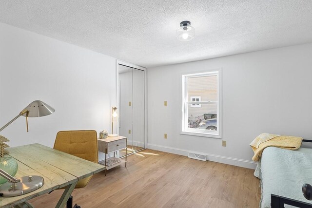 office area with a textured ceiling, light wood finished floors, visible vents, and baseboards