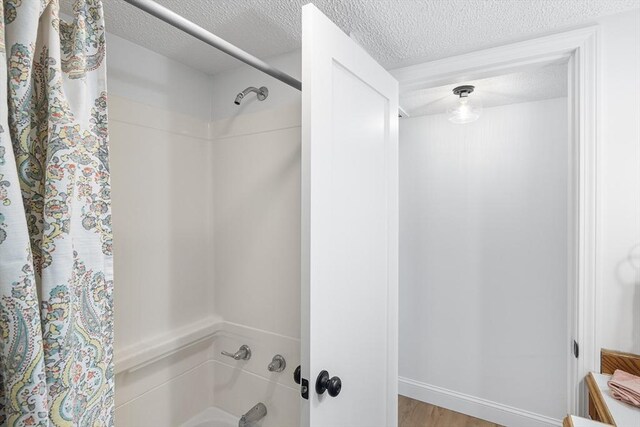 bathroom with shower / bathtub combination with curtain, a textured ceiling, and wood finished floors