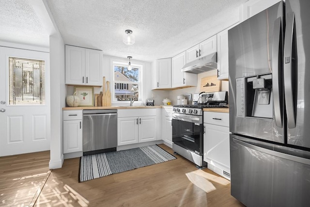 kitchen with light wood-style flooring, decorative light fixtures, stainless steel appliances, under cabinet range hood, and white cabinetry