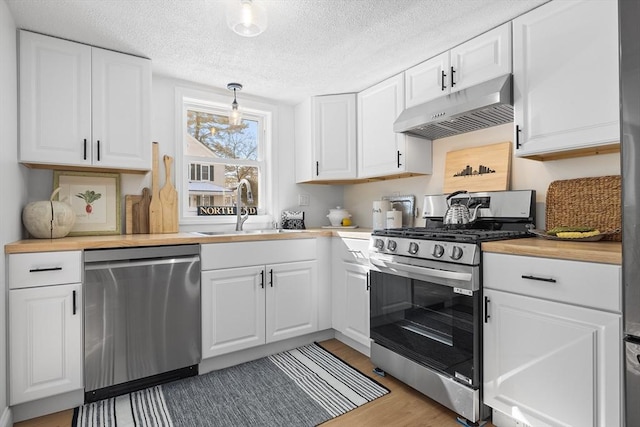 kitchen featuring hanging light fixtures, stainless steel appliances, under cabinet range hood, white cabinetry, and a sink