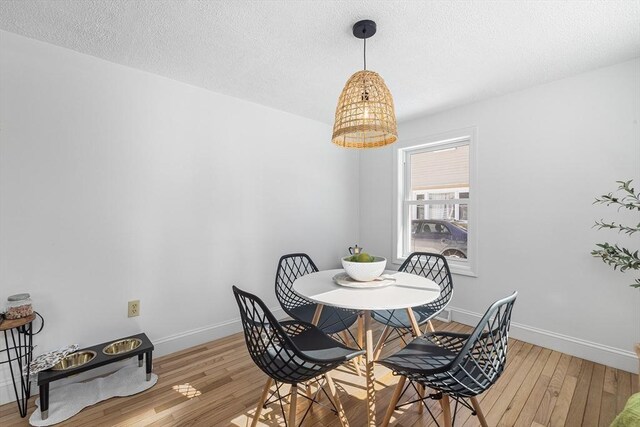 dining room with a textured ceiling, light wood-style flooring, and baseboards