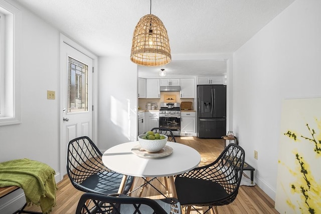 dining room featuring light wood-style flooring, baseboards, and a textured ceiling