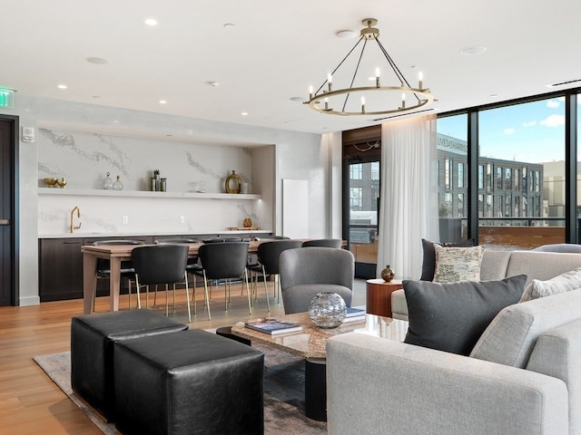 living room with a chandelier, indoor bar, light hardwood / wood-style flooring, and a wall of windows