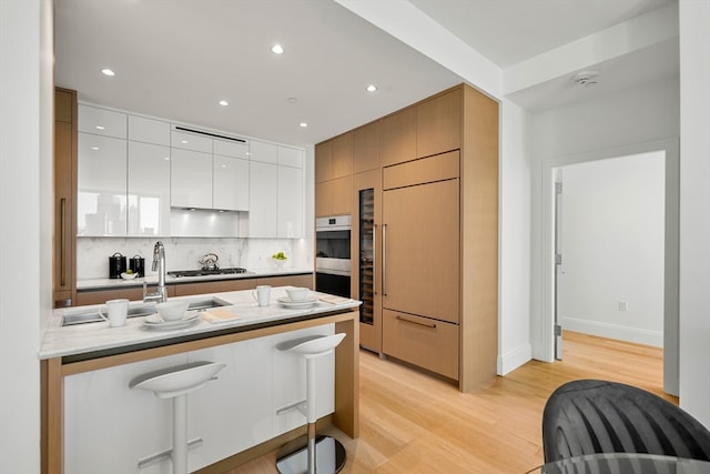 kitchen featuring light wood-type flooring, backsplash, a breakfast bar, stainless steel appliances, and white cabinets