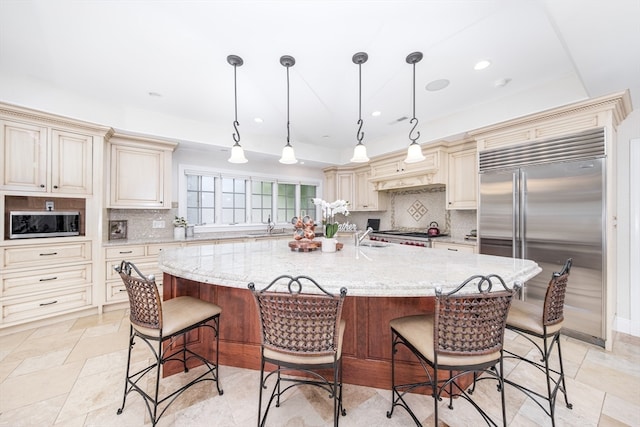 kitchen featuring cream cabinets, stainless steel appliances, a center island with sink, and pendant lighting