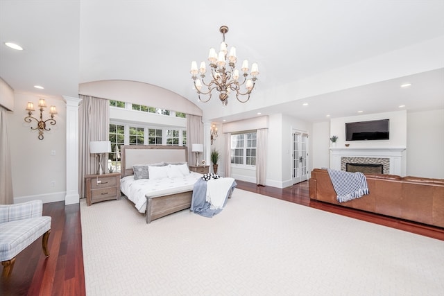 bedroom with lofted ceiling, an inviting chandelier, dark hardwood / wood-style floors, a tile fireplace, and ornate columns