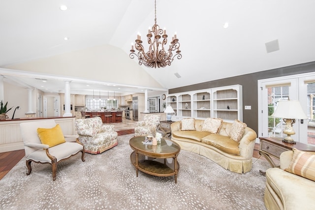 living room featuring decorative columns, high vaulted ceiling, a notable chandelier, and wood-type flooring